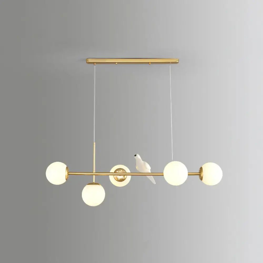 Decorbites modo island 5-light pendant light with gold-toned finish, frosted glass globes, and milk white ceramic bird figurine