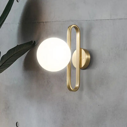 Modern gold wall lamp with opal glass sphere and single light featuring a sleek curved metal frame for bedroom use