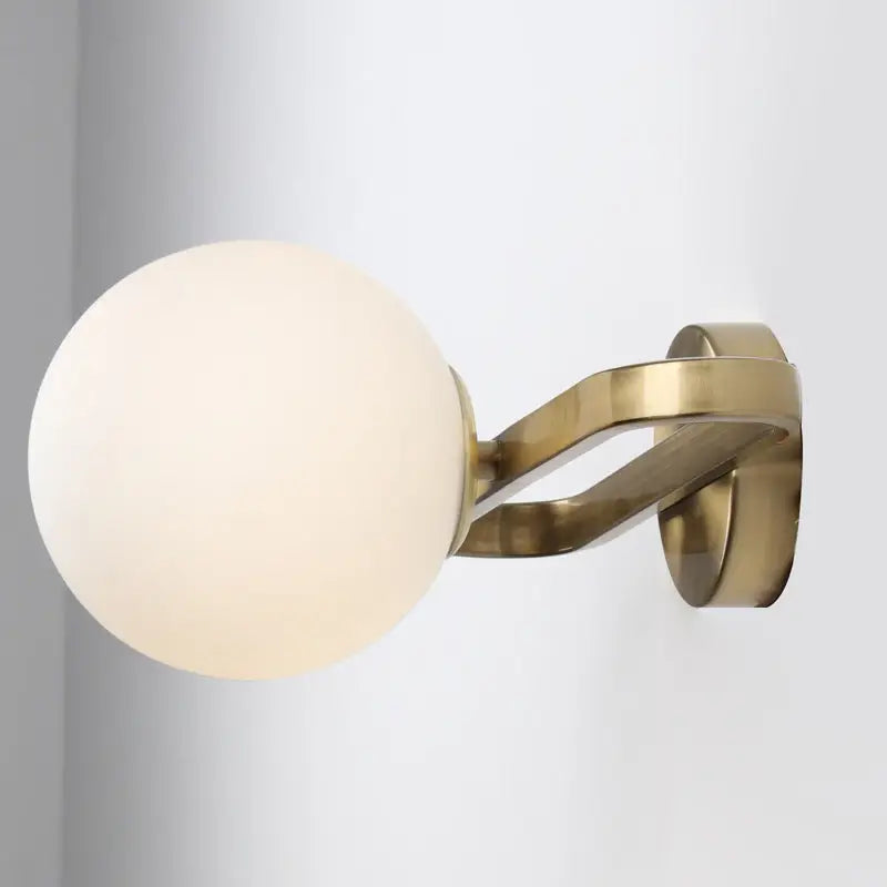 A sleek modern gold wall lamp with a smooth opal glass sphere single light for bedroom use