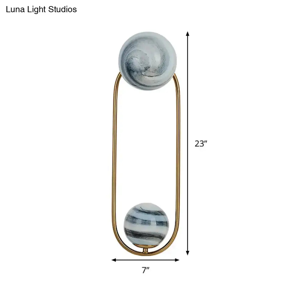 Modern gold oval wall sconce light fixture with two polished marble spheres on a slender metal frame for living room use