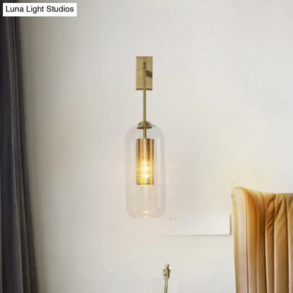 Modern gold perforated sconce with clear glass cylinder and illuminated brass wall light for bedroom use