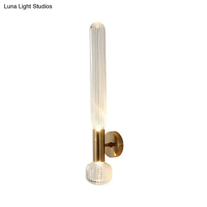 Modern gold ribbed glass wall lighting fixture with a tall cylinder and spherical base illuminated by warm light