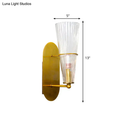 Modern gold wall sconce with clear vertically ribbed glass shade designed as a bedroom wall light