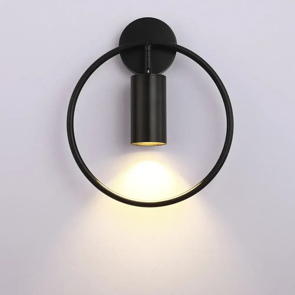 Black circular wall sconce light with matte metal ring and cylindrical fixture for modern bedroom lighting