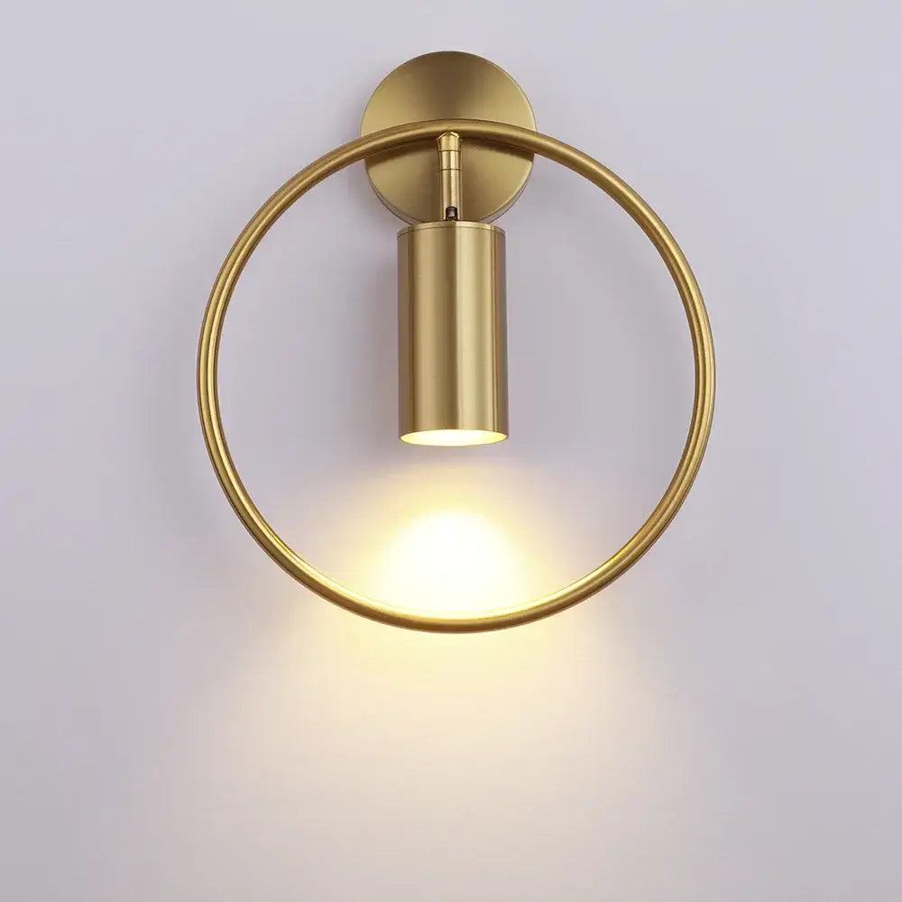 Gold-toned modern wall sconce light with a sleek cylindrical LED fixture and polished metal ring for bedroom use