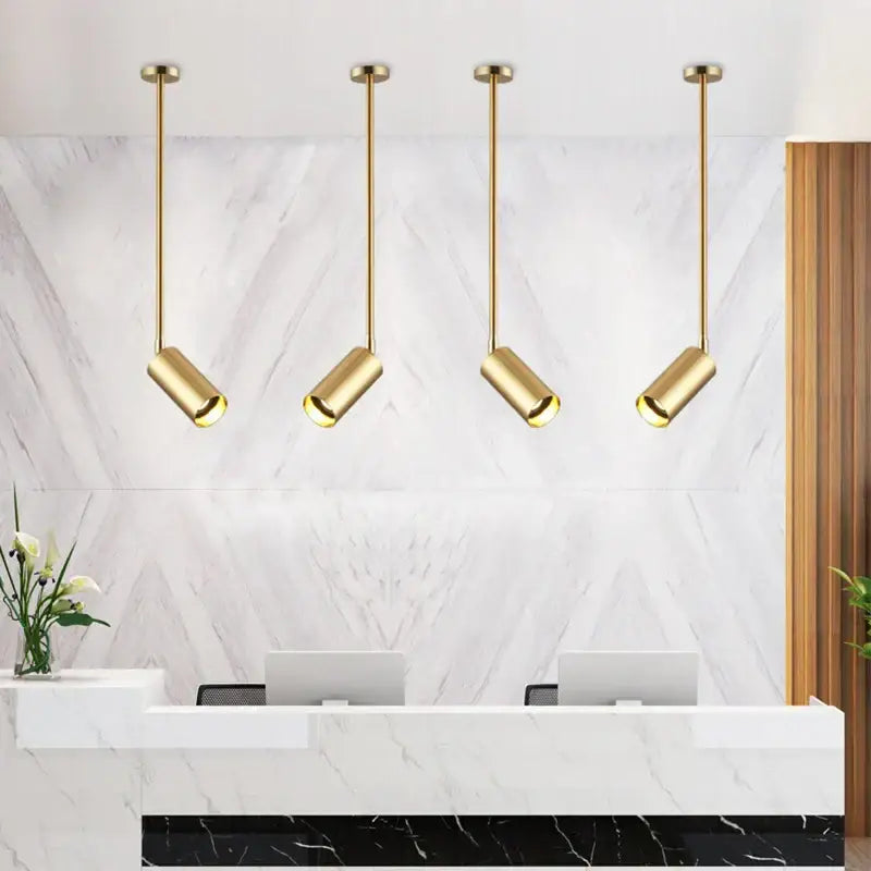 Four sleek gold finished modern rotating led spotlights with cylindrical shades hang above the reception desk