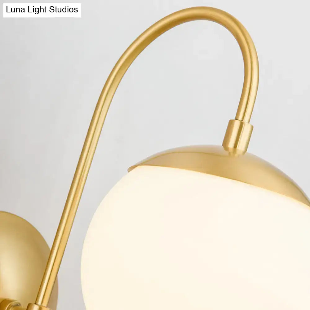 Modern gold round wall lamp featuring a gold-toned spherical opal glass shade with a curved brass arm for bedroom use