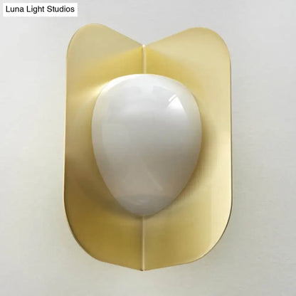 Modern gold sconce light with a gold-toned curved metal shade and smooth white oval glass for bedroom illumination