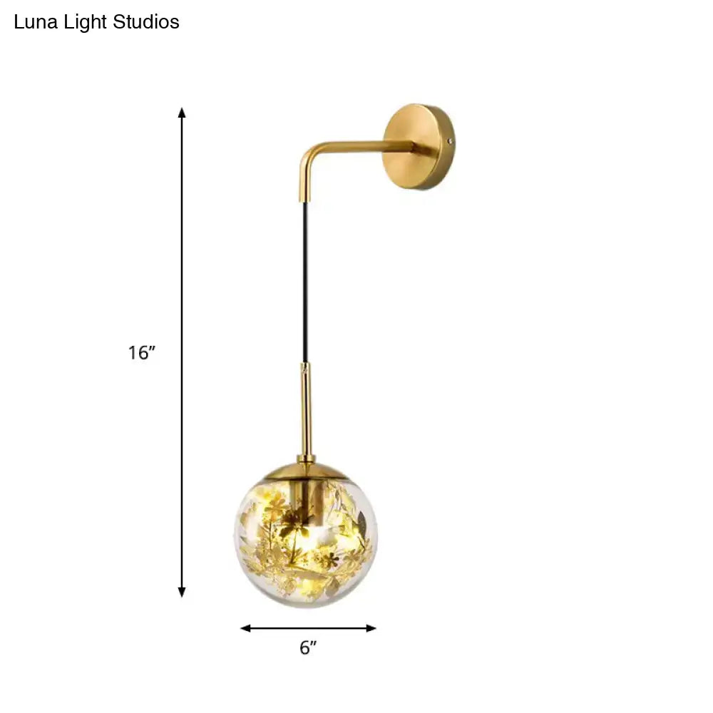 Modern gold shattered leaf light fixture featuring a clear glass globe with embedded golden floral elements illuminated interior