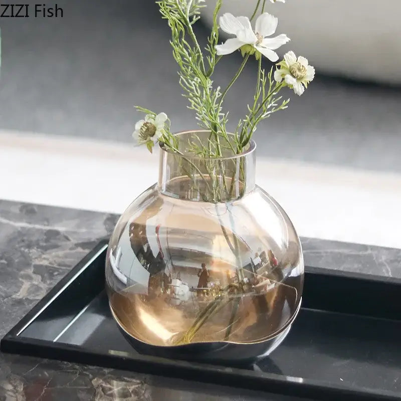A sleek transparent glass vase with rounded body and narrow neck holding white flowers for decorbites amber glass decor