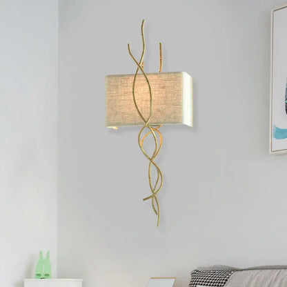 Modern gold wall mount light with gold-toned wrought iron and beige linen shade for bedroom use