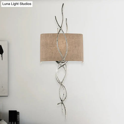 Silver twisted metal wall mount light with beige fabric shade in a modern gold silver branch design for bedrooms