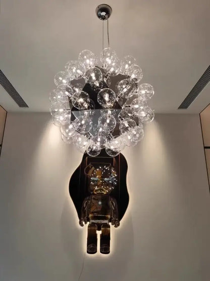 A modern gold and silver clear glass bubble chandelier with numerous clear glass bulbs above a dark-framed bear sculpture