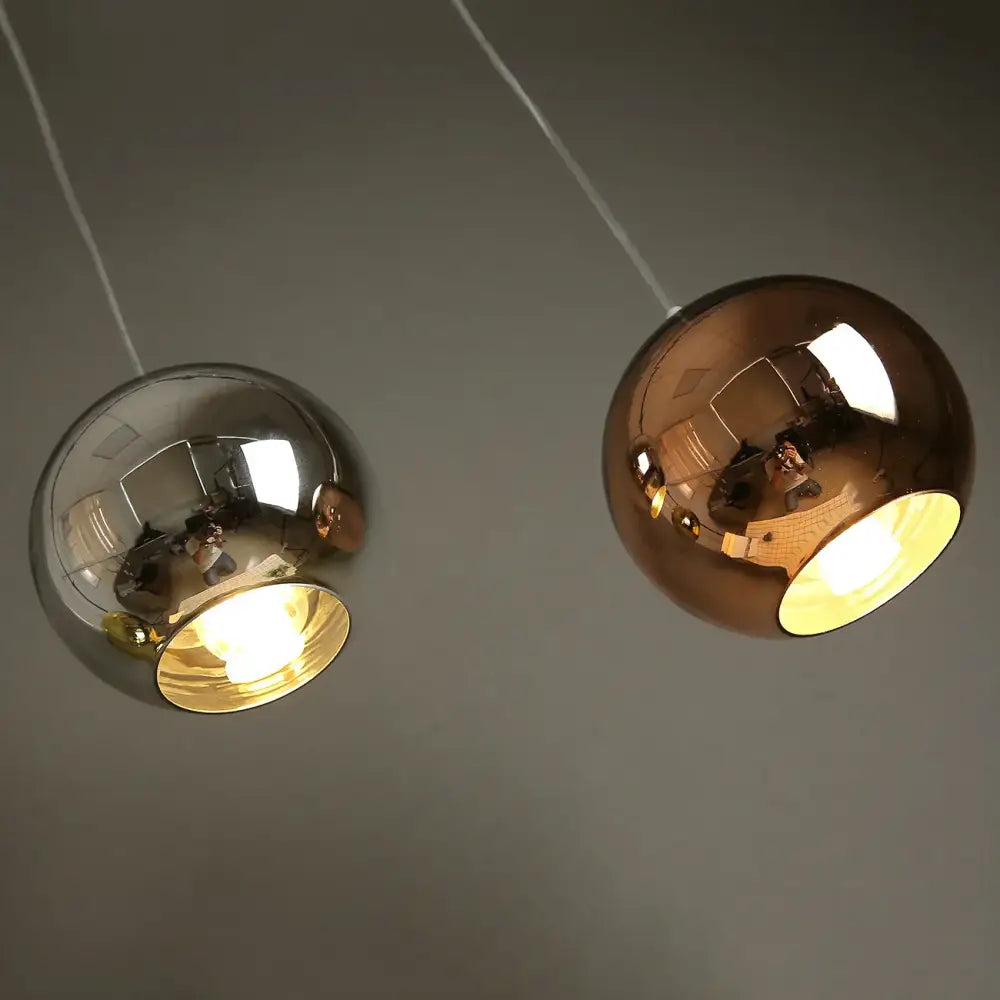 Two glass bubble ball pendant lights with polished chrome and rose gold finishes featuring illuminated interiors