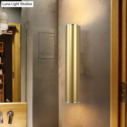 A sleek cylindrical gold tube wall mounted sconce with polished brass finish for modern corridor lighting