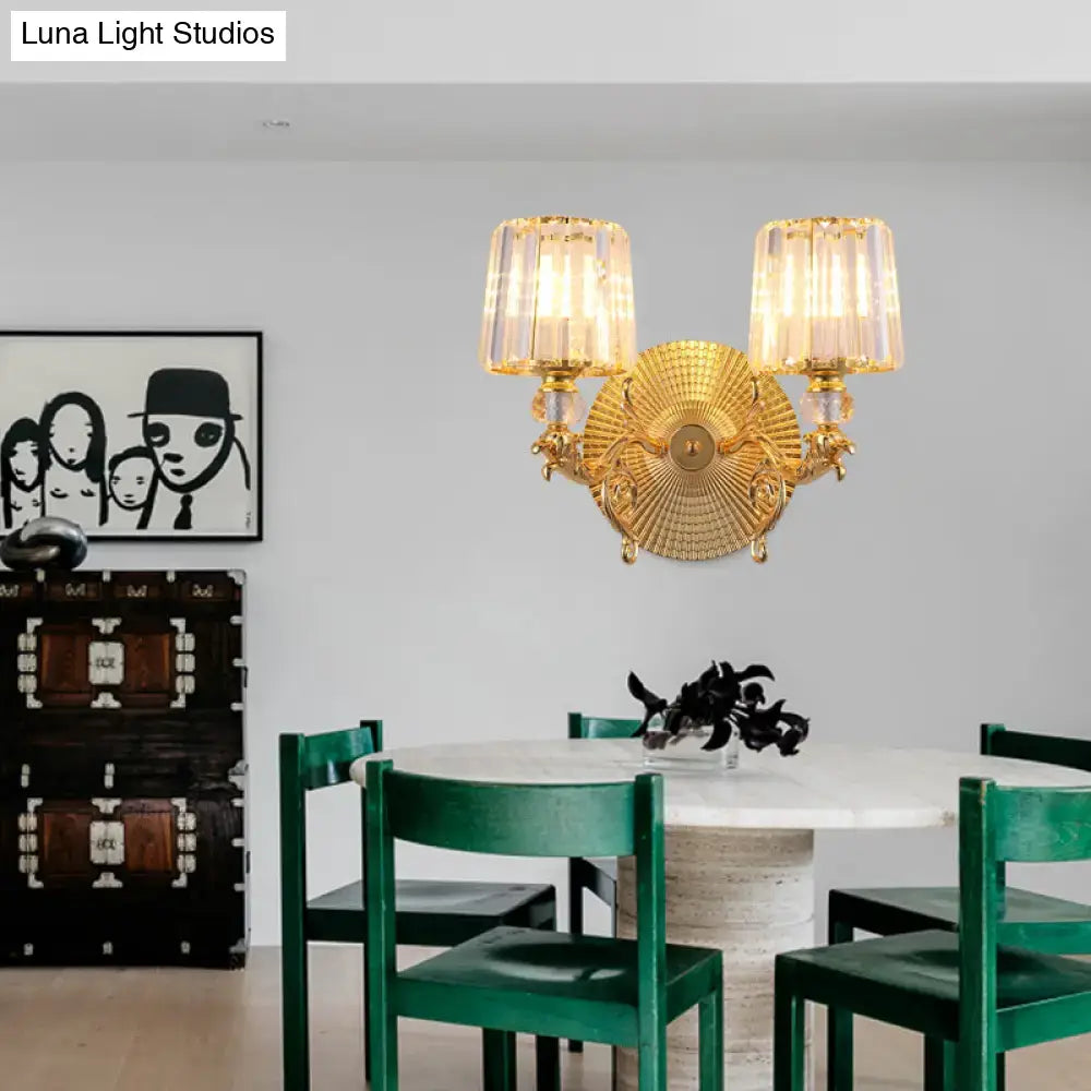 Modern gold tapered wall light fixture with two fluted crystal shades and ornate sunburst-patterned central plate