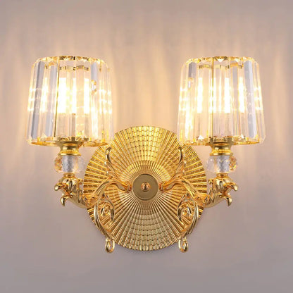 Modern gold tapered wall light fixture featuring ornate gold finish with two crystal-encased light fixtures and sunburst design