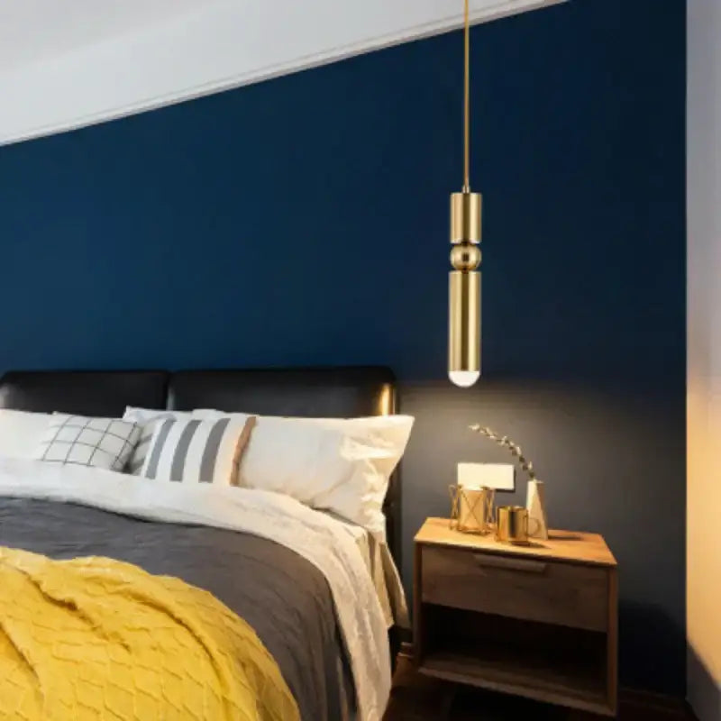 A sleek cylindrical gold tube pendant light from decorbites hangs above the bed as elegant bedside decor