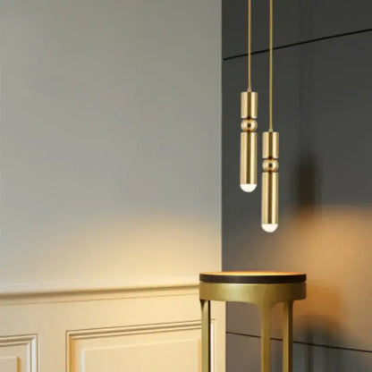 Two elegant gold tube pendant lights with cylindrical segmented design hang above a matching decorbites gold tube stool