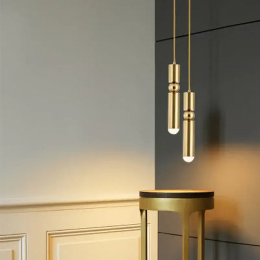 Two elegant gold tube pendant lights with cylindrical segmented design hang above a matching decorbites gold tube stool