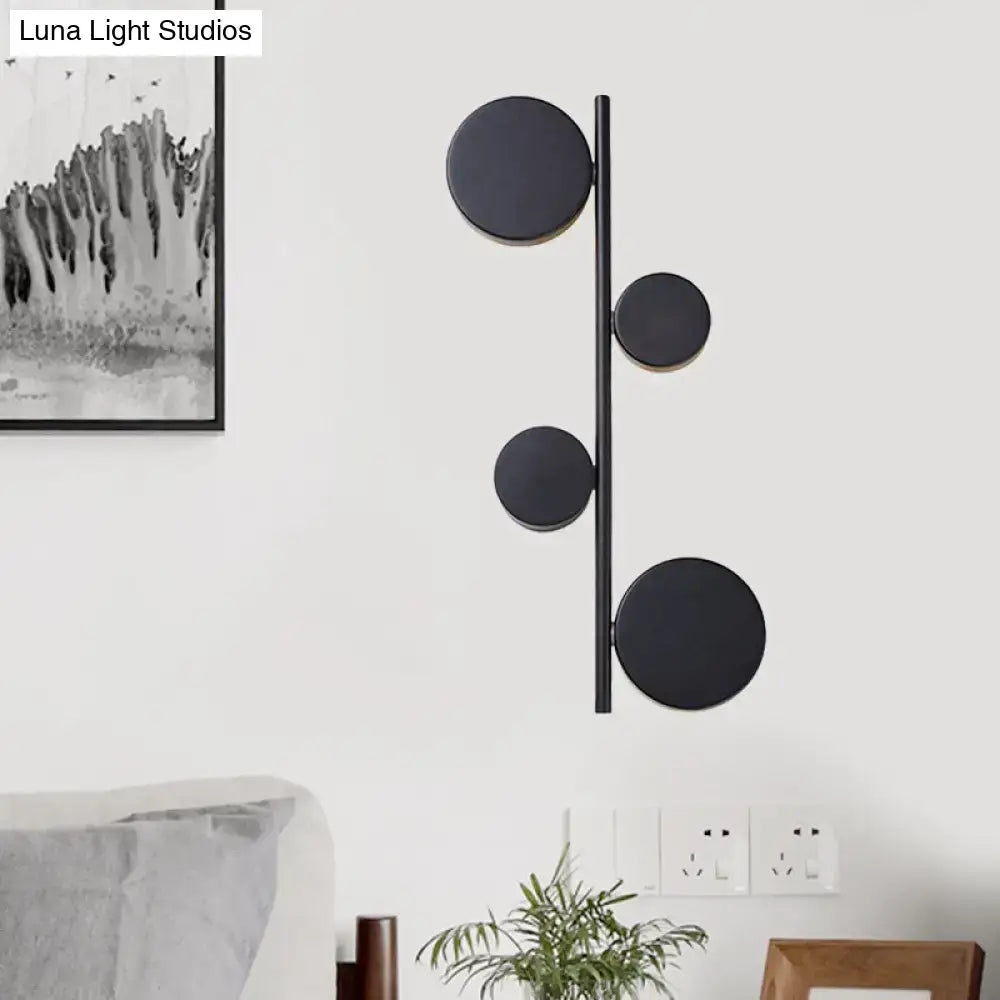 Modern black gold finish vertical linear sconce light with four circular discs on a slender rod for living room use