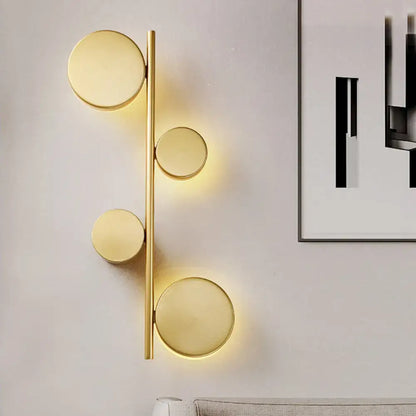 Modern gold vertical linear sconce light with four circular glowing fixtures in black gold finish for living room use