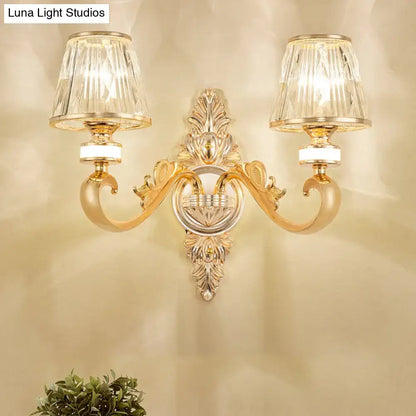 Modern gold wall lamp fixture with two crystal cone shades and intricate leafy gold wall detailing for bedroom sconce