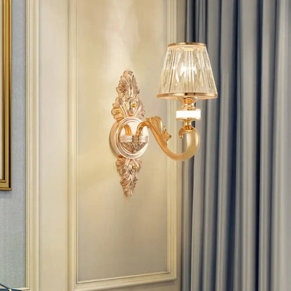 Gold wall lamp fixture featuring an ornate gold-toned design with a faceted crystal block gold cone shade for bedroom use