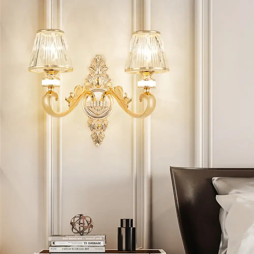 Gold wall lamp fixture with ornate design and two crystal cone shades for elegant bedroom sconce lighting
