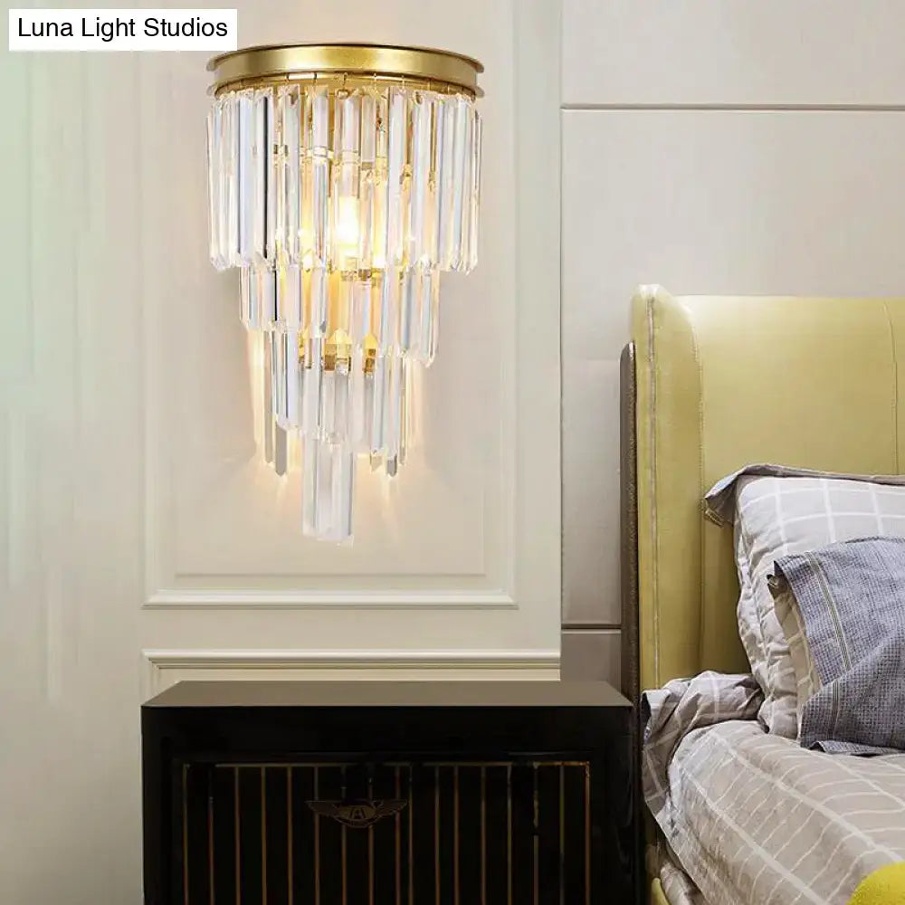 Modern gold wall lamp featuring a gold-toned sconce with cascading clear crystal block prisms for bedroom use