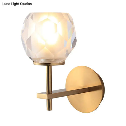 A warm glowing modern gold wall lamp with faceted globe shade and brass arm as wall mounted light for hallway