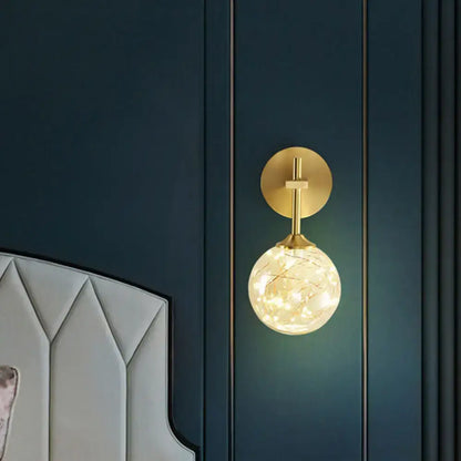 Modern gold wall lamp with a gold-toned spherical glass shade and warm led fairy lights for bedroom lighting