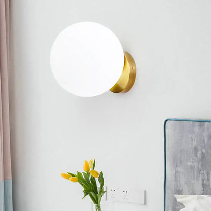Modern gold wall lamp with frosted opal glass spherical shade and polished brass base for bedroom lighting