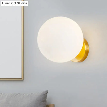 Modern gold wall lamp with opal glass shade featuring a frosted spherical design mounted on a polished metal base