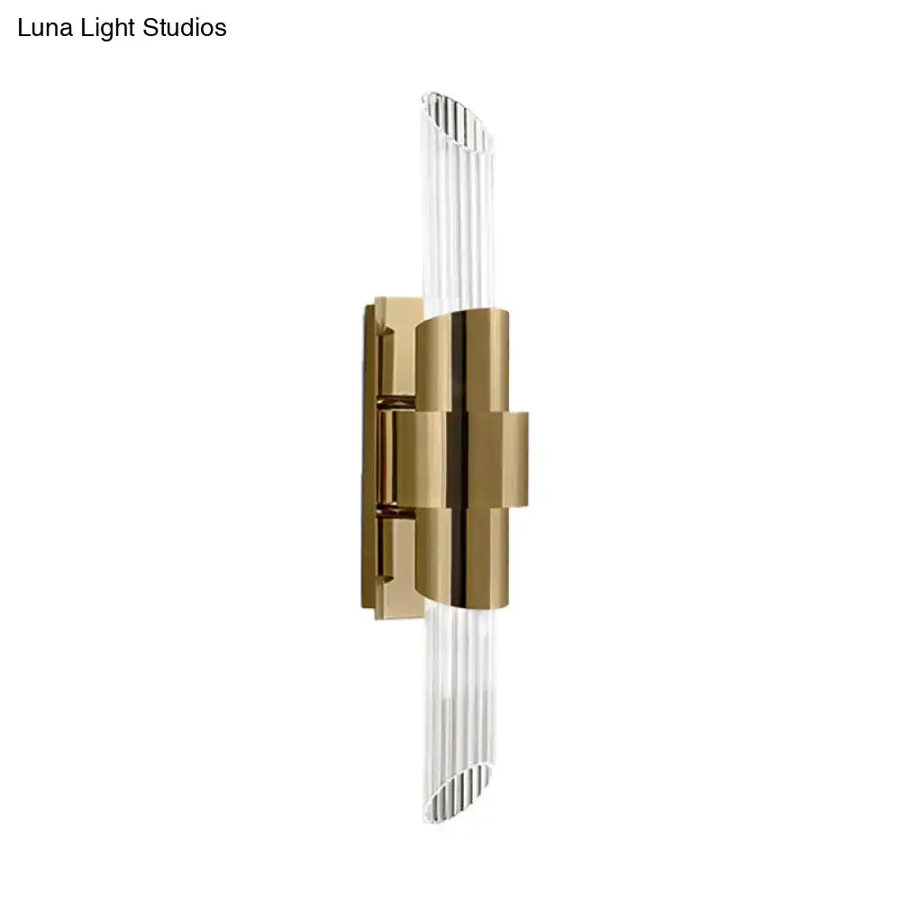 Modern gold wall lamp with sleek metal frame and clear vertically ribbed prismatic crystal shade for bedroom lighting