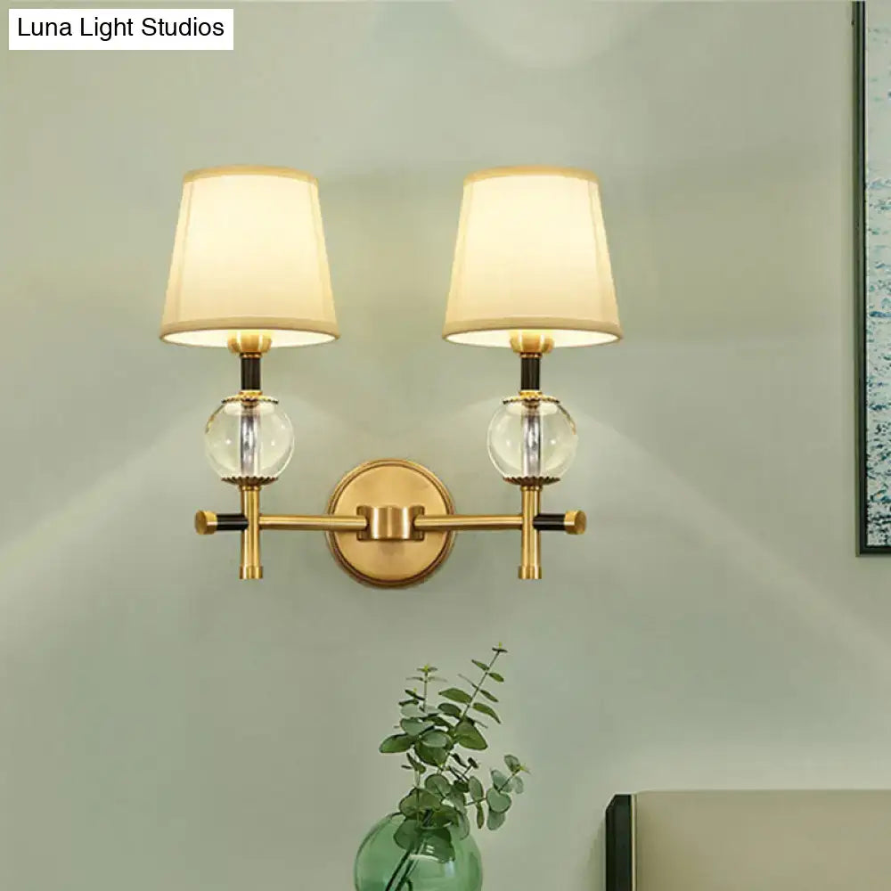 Modern gold wall light featuring a brass finish, two cream conical fabric shades, and clear glass globe accents for bedrooms