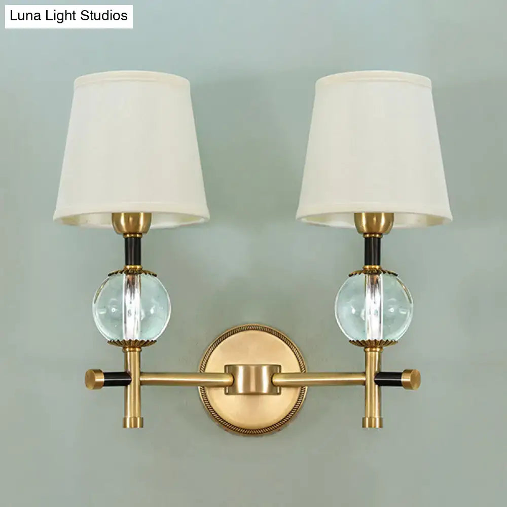 Modern gold wall light with brass finish, two conical fabric shades, and clear glass globe accents for bedroom use