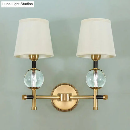 Modern gold wall light with brass finish, two conical fabric shades, and clear glass globe accents for bedroom use