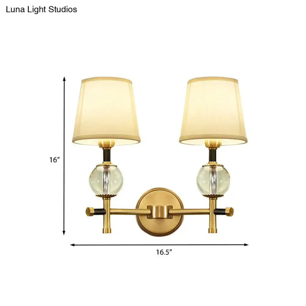 Modern gold wall light with fabric shade featuring two clear glass globes and cream-colored conical fabric shades for bedroom