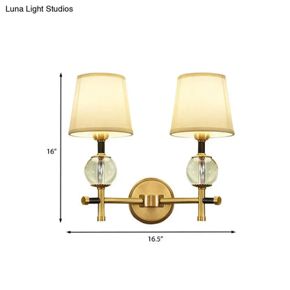 Modern gold wall light with fabric shade featuring two clear glass globes and cream-colored conical fabric shades for bedroom