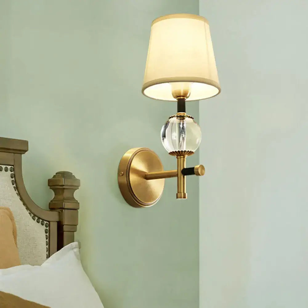 Modern gold wall light with clear crystal globe and conical fabric shade ideal for bedroom lighting