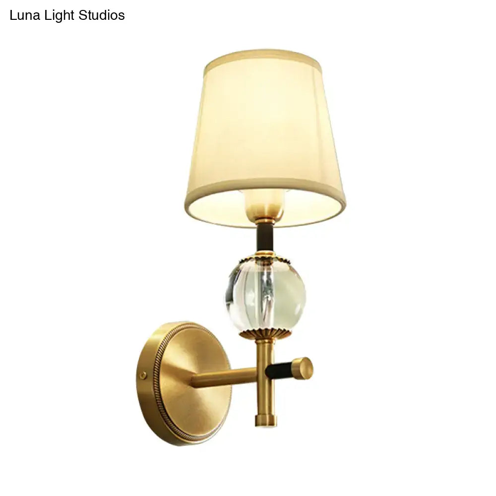 Modern gold wall light featuring a gold-toned sconce with a faceted crystal globe and a conical fabric shade