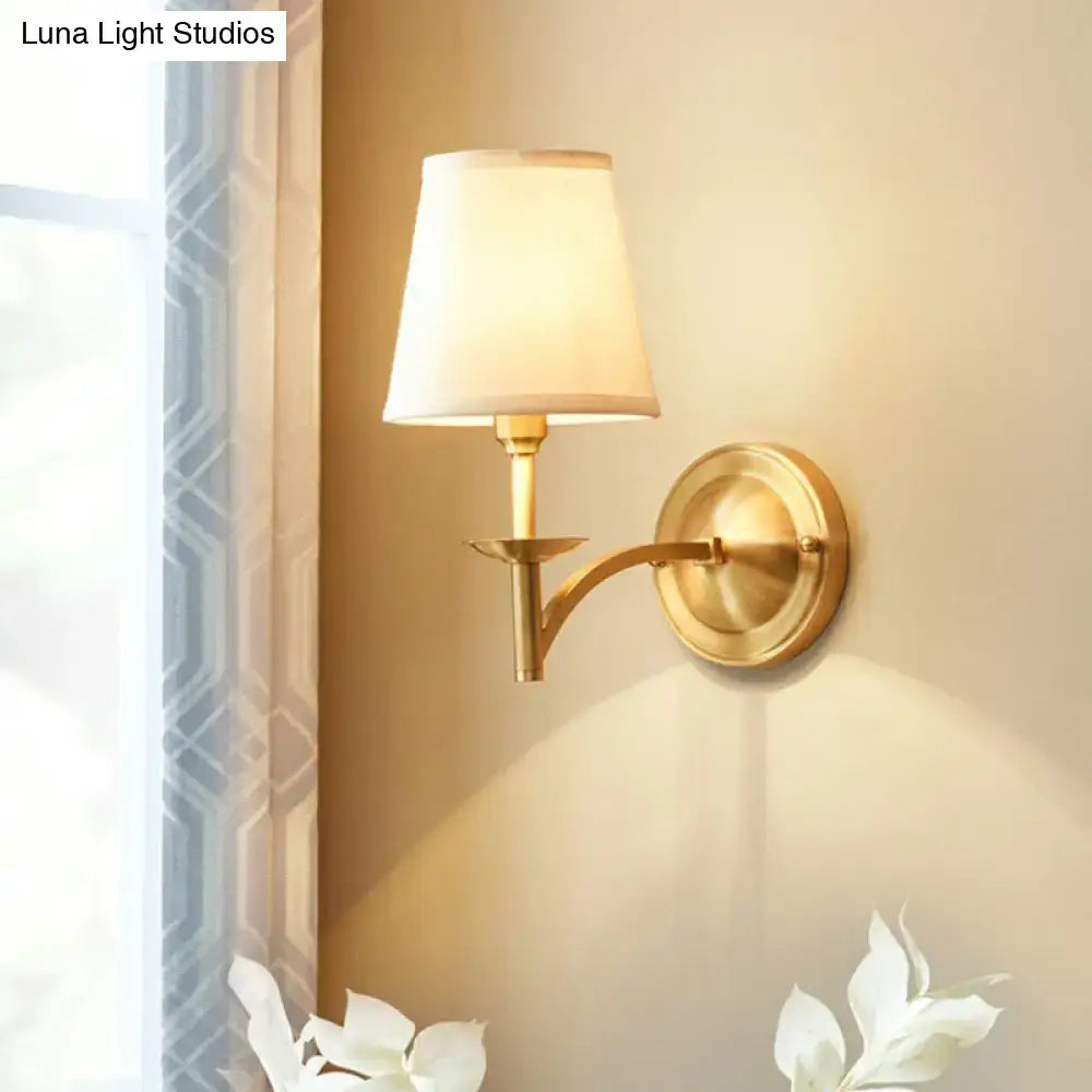 Modern gold wall light with cream fabric shade featuring a gold-finished frame and suitable fixture width for bedroom use