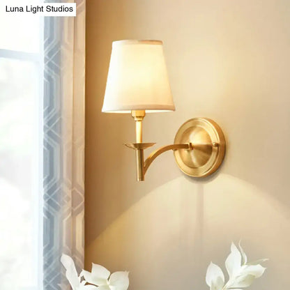 Modern gold wall light with cream fabric shade featuring a gold-finished frame and suitable fixture width for bedroom use