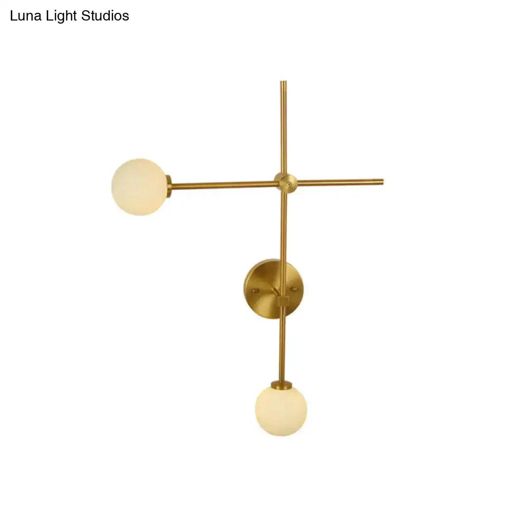 Brass-finished modern gold wall mount lamp with two frosted closed glass globes in a minimalist crossed wall mount design