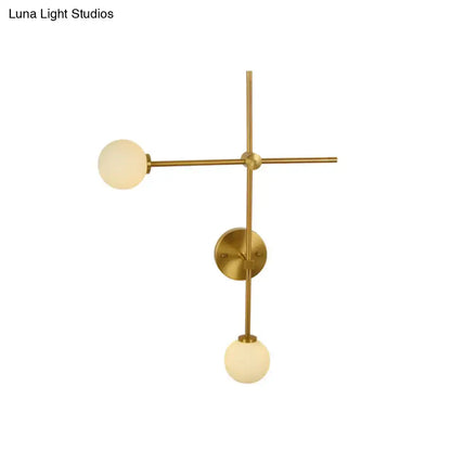 Brass-finished modern gold wall mount lamp with two frosted closed glass globes in a minimalist crossed wall mount design