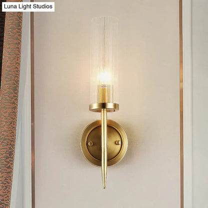 Modern gold wall sconce with clear ribbed glass cylinder housing an illuminated led bulb for 110v-120v use