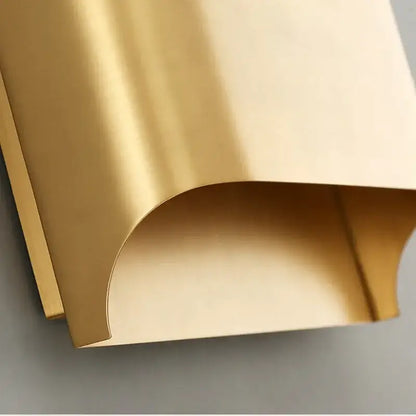 A sleek gold wall sconce with a curved metal panel featuring a smooth reflective surface by decorbites copper brass