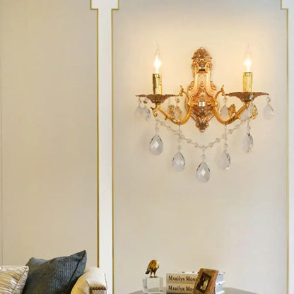 Modern gold wall sconce with crystal drops featuring two lit e12 e14 candle-style bulbs for elegant bedroom lighting