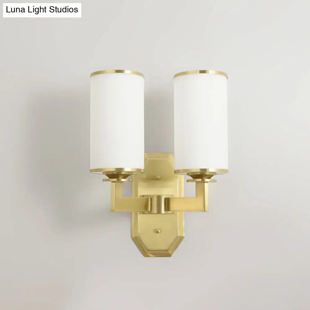 Modern gold wall sconce with two cylindrical opal glass shades for bedroom lighting fixture